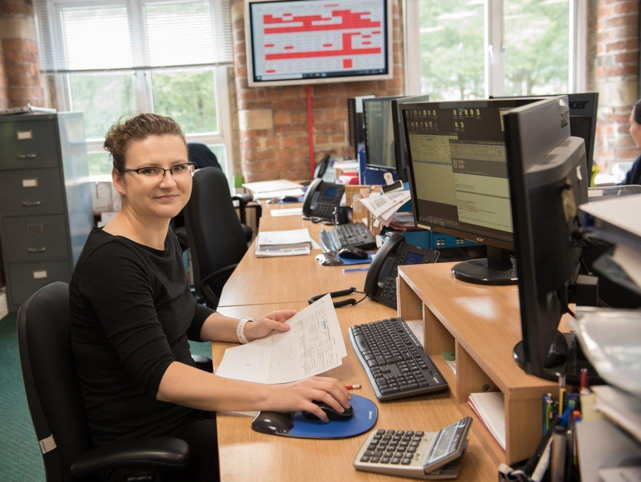 woman sat in office at desk with two computer monitors